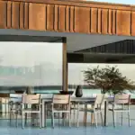 Karmstolar DELIA i khaki runt ett rektangulärt utebord i eftermiddagssol.