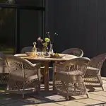 CIRCUS matbord natur teak från Brafab med sex karmstolar i konstrotting på uteplats i kvällsljus.