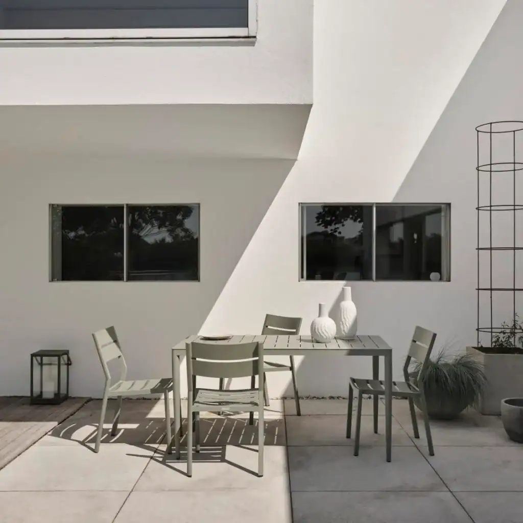 DELIA matstolar i dusty green i solbelyst uteplats med modern fasad.