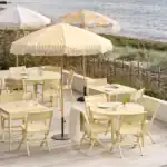 Uteservering med DELIA matstolar i lemon under färgglada parasoller vid havet.