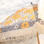 Närbild på Gatsby parasoll blommig 185 cm från Brafab med retroblommor i gult, svartprickigt mönster och dekorativa fransar.