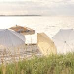 Flera strandparasoller inklusive Gatsby parasoll blommig 185 cm från Brafab uppställda i sanden vid solnedgången.