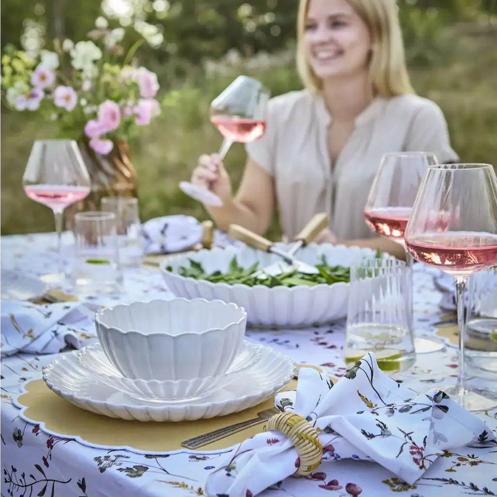 Kvinna vid sommarbord håller rödvinsglas NOMI med rosévin.