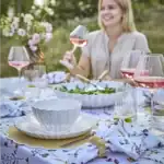 Kvinna vid sommarbord håller rödvinsglas NOMI med rosévin.