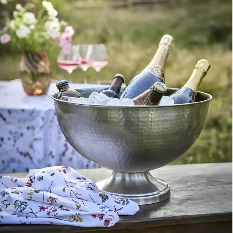 Servetter FLORA ligger vikta på ett bord bredvid en metallisk champagnekylare fylld med is.