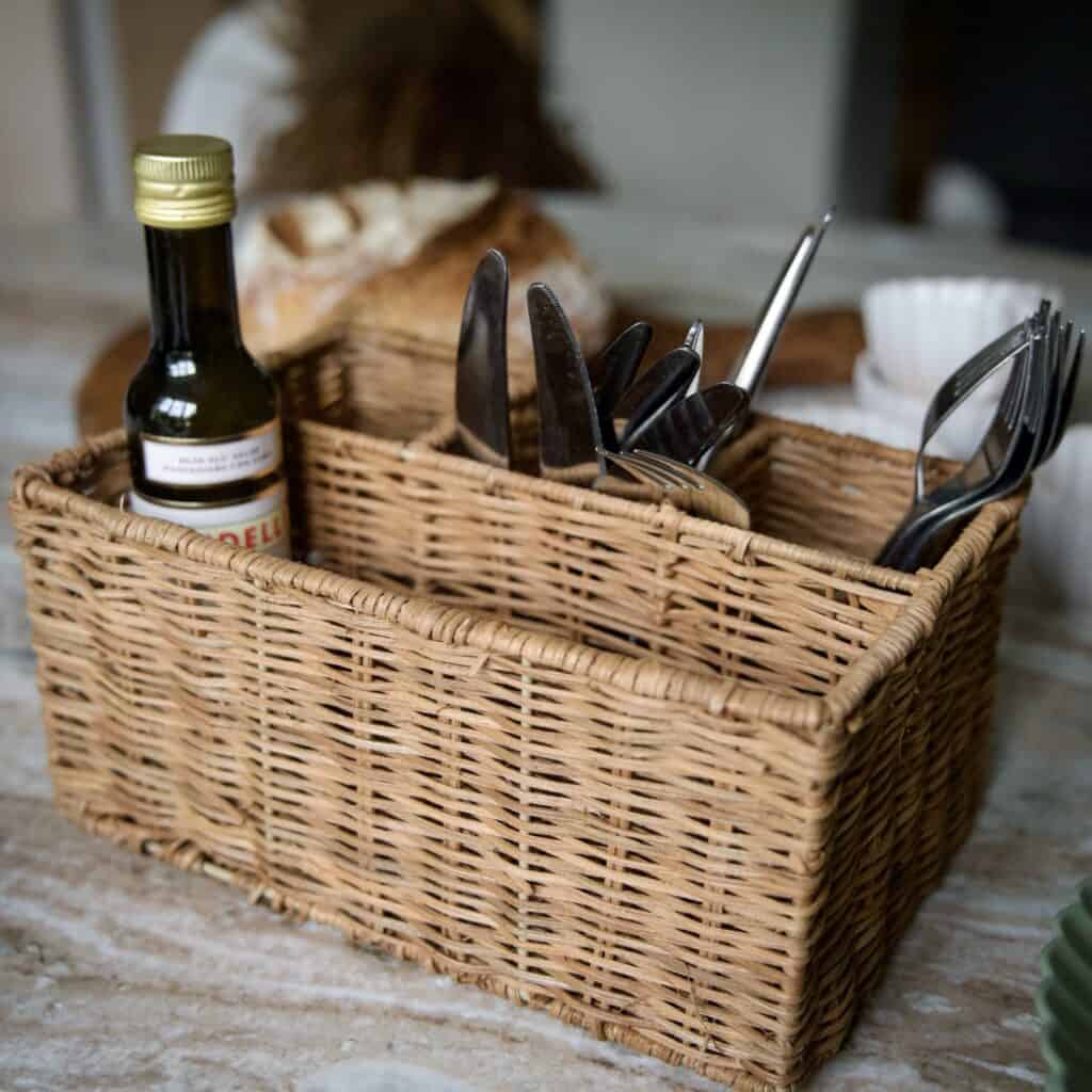Förvaringskorg i rotting med sex fack från Madam Stoltz, använd som bestickkorg på dukat bord med olivolja och bröd.
