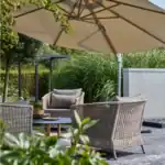Två beige fåtöljer Brafab Aster i en trädgårdsmiljö under stort parasoll