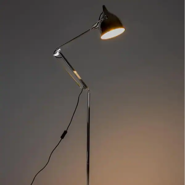 Golvlampa READER i krom från Zuiver, tänd i ett mörkt rum som skapar en varm och inbjudande atmosfär.