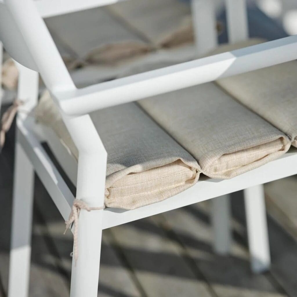 Närbild på sitsen på vit karmstol Delia från Brafab med beige sittdyna i linnekänsla.