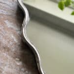 Detaljbild av spegeln Jonna med vågig kant och silverfärgad ram, en elegant inredningsdetalj från Hemlängtan.