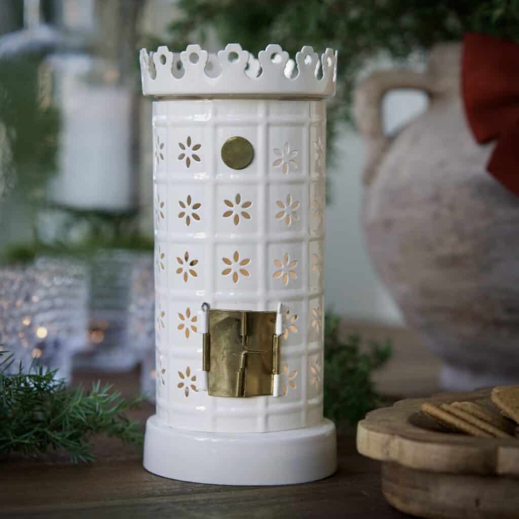 Vit ljuslykta formad som en kakelugn med utskurna blommönster, tänd i miljöbild.