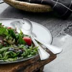 CARUM salladsbestick i vintage stil från Nordal på ett serveringsfat med färsk sallad och bär