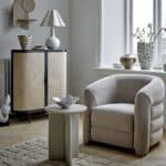 Skandinaviskt vardagsrum med skänk i svart metall och rotting från Bloomingville, kombinerat med fåtölj i beige sammet och ljusa inredningsdetaljer. Finns hos Hemlängtan.