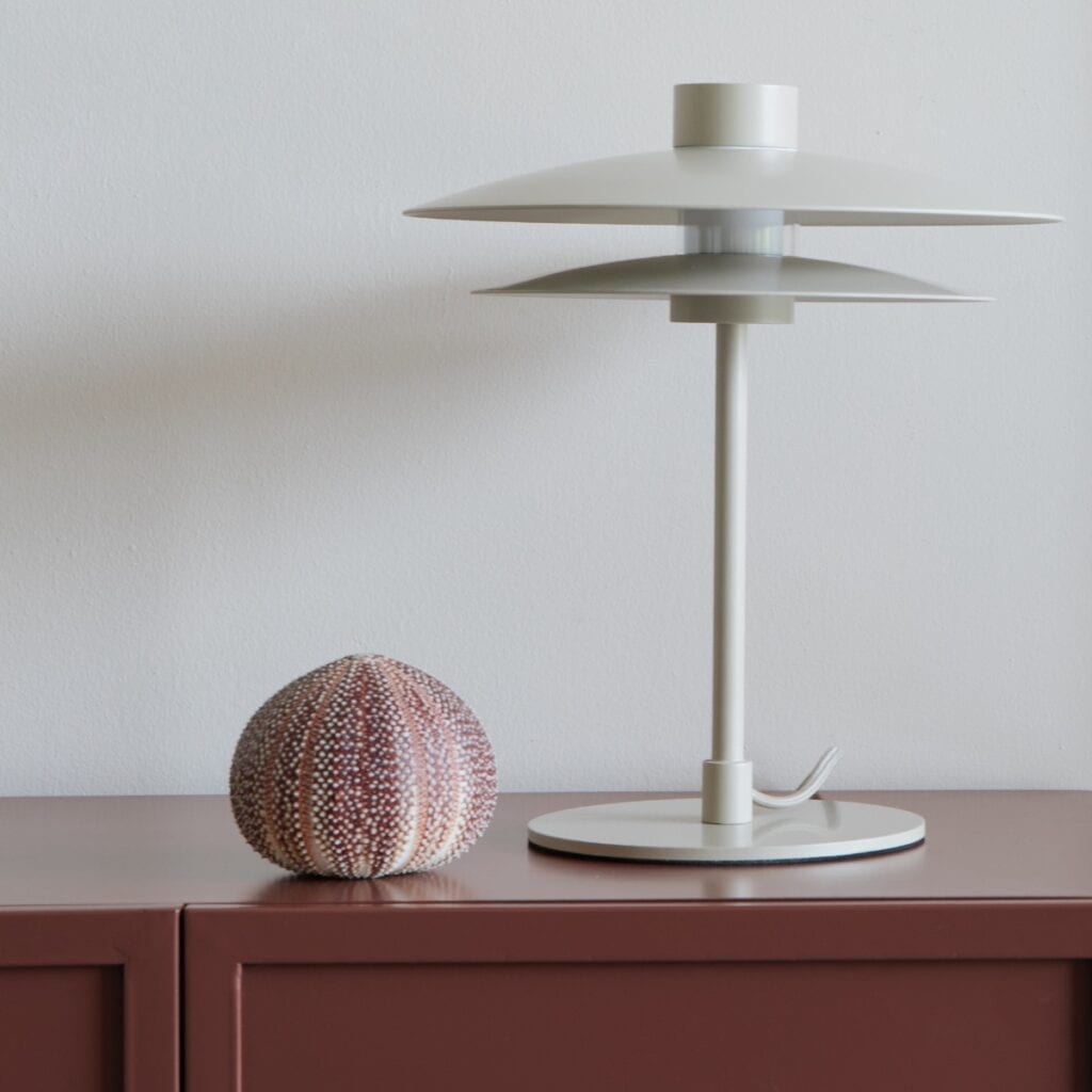 Bordslampa WUBBO beige från Hemlängtan, placerad på ett skåp med stilren design som sprider mjukt ljus.