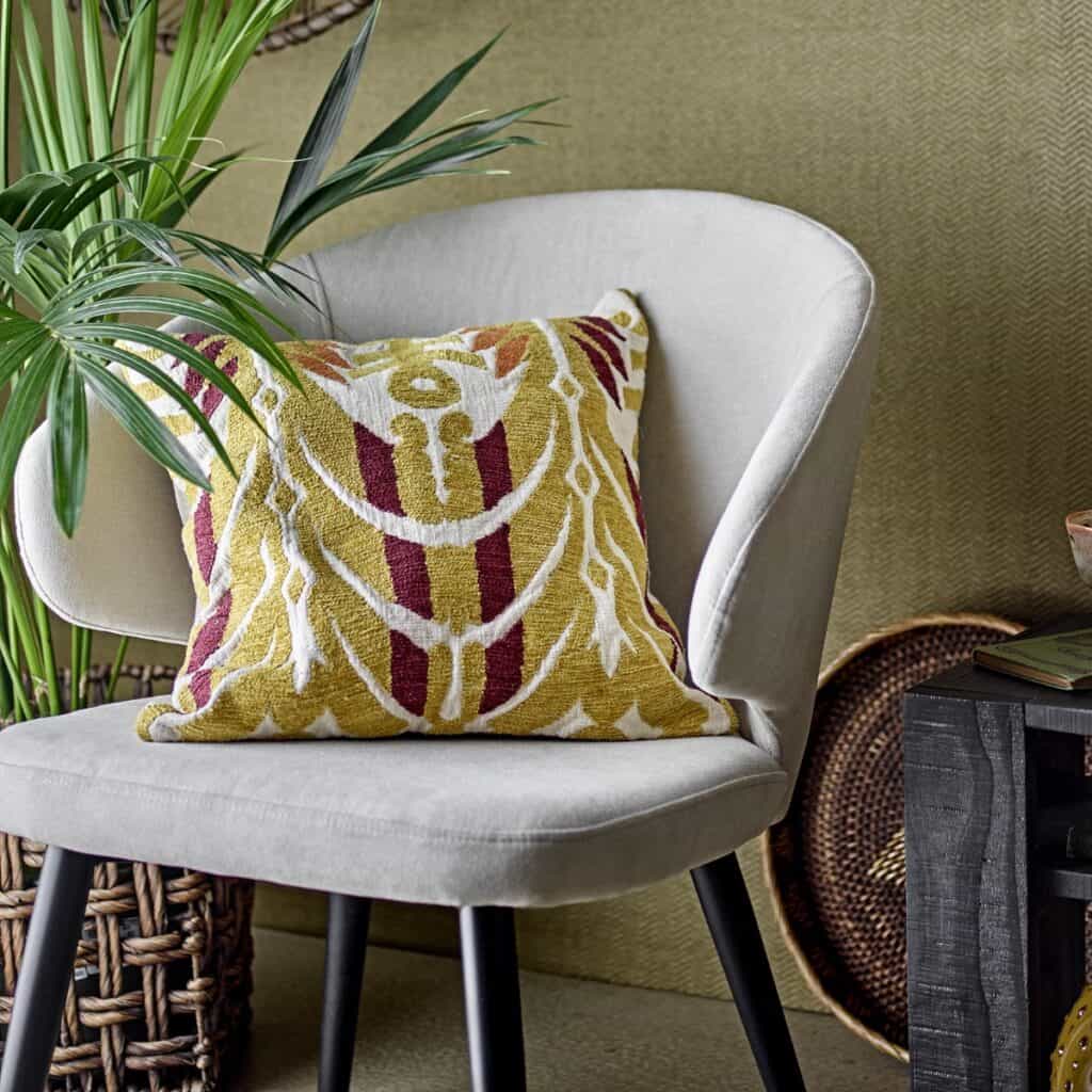 Stol Loon Beige Bloomingville – lounge-stol i beige tyg med svarta ben, stylad med mönstrad kudde i gult och rött i en modern inredning.