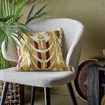 Stol Loon Beige Bloomingville – lounge-stol i beige tyg med svarta ben, stylad med mönstrad kudde i gult och rött i en modern inredning.