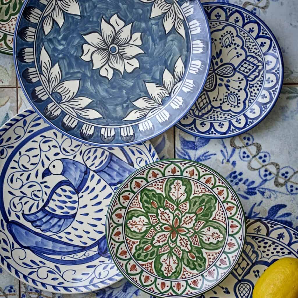 Färgstarka handmålade tallrikar i stengods från Bloomingville i blått, grönt och rött mönster, med citron i förgrunden mot kakelbakgrund.