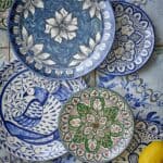 Färgstarka handmålade tallrikar i stengods från Bloomingville i blått, grönt och rött mönster, med citron i förgrunden mot kakelbakgrund.