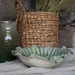 Skål IVY grön terrakotta dekorativ med vågig kant från Wikholm Form i miljö med flätad korg och grön vas