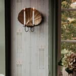 Väggljusstake Snäckan i antik mässing från Strömshaga med två tända kronljus på vägg med mönstrad tapet.