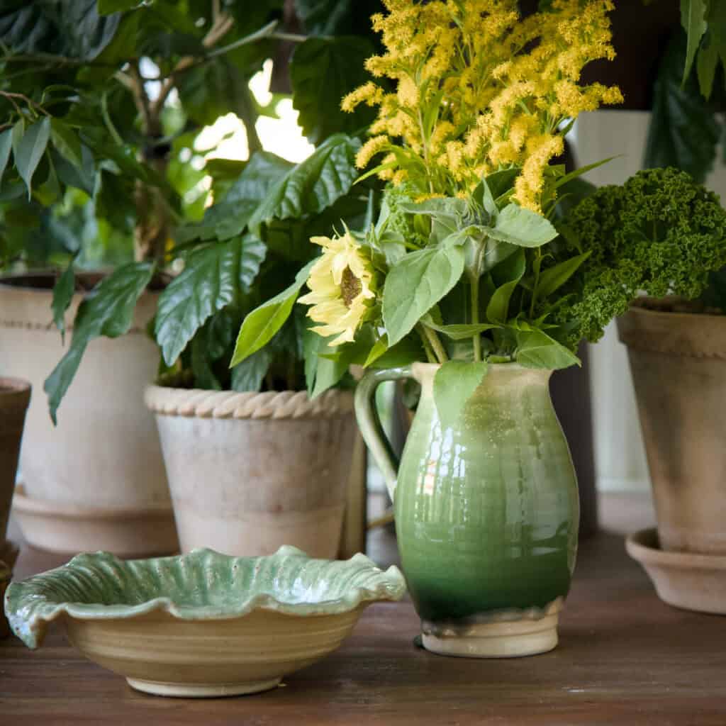 Vas Ivy grön från Wikholm form i glaserad keramik, använd som kanna med bukett solrosor och gula blommor.