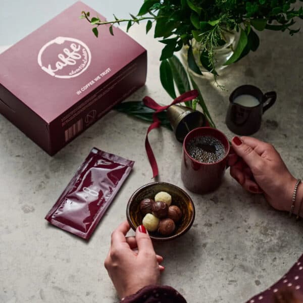 Nabos vinröda kaffeadventskalender på stenbord med kopp kaffe, chokladpraliner och gröna kvistar i bakgrunden.