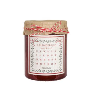 Kalenderljus i mörkrött glas med doft av äpple och kanel, placerat på träbord med grön mossa – julig stämning från Strömshaga.