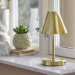 Laddningsbar LED-lampa i mässing från Bloomingville, Lianna – placerad på ett fönsterbräde i naturligt dagsljus.