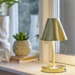 Laddningsbar lampa i mässing från Bloomingville, Lianna – står på ett fönsterbräde och sprider varmt ljus.