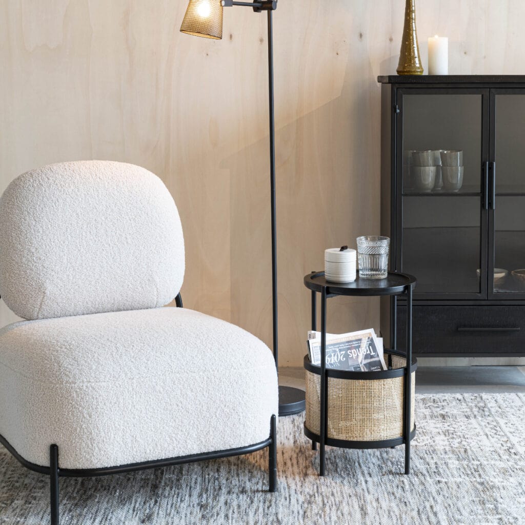 Svart sidobord i metall och rotting bredvid fåtölj i ljust tyg – Makoto från Hemlängtan i vardagsrumsmiljö.