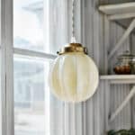 Taklampa Marit i mässing och beige opalglas hängande i fönster – sprider varmt ljus med klassisk charm.