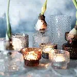 DOTTI ljuslyktor i olika färger med blommor och levande ljus i en stämningsfull miljö.