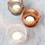 Tre DOTTI ljuslyktor i klart, grått och amberglas på marmorbord med tända värmeljus.