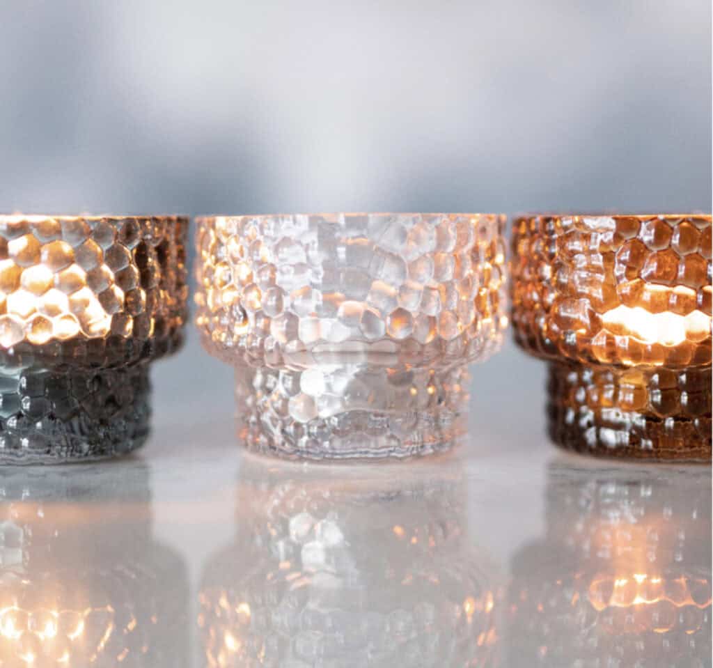 DOTTI ljuslyktor i klart, amber och grått glas i rad på blank yta med reflektioner.