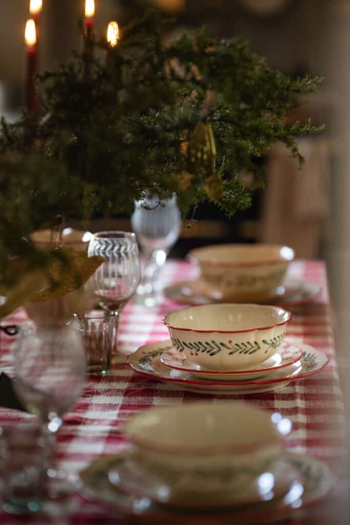 Lantlig juldukning med porslin i rött och grönt, rödvitrutig duk och mässingsljus i bakgrunden.