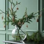 Halmdekorationer till jul hängande på grankvist i glasvas – naturlig julinredning i skandinavisk stil.