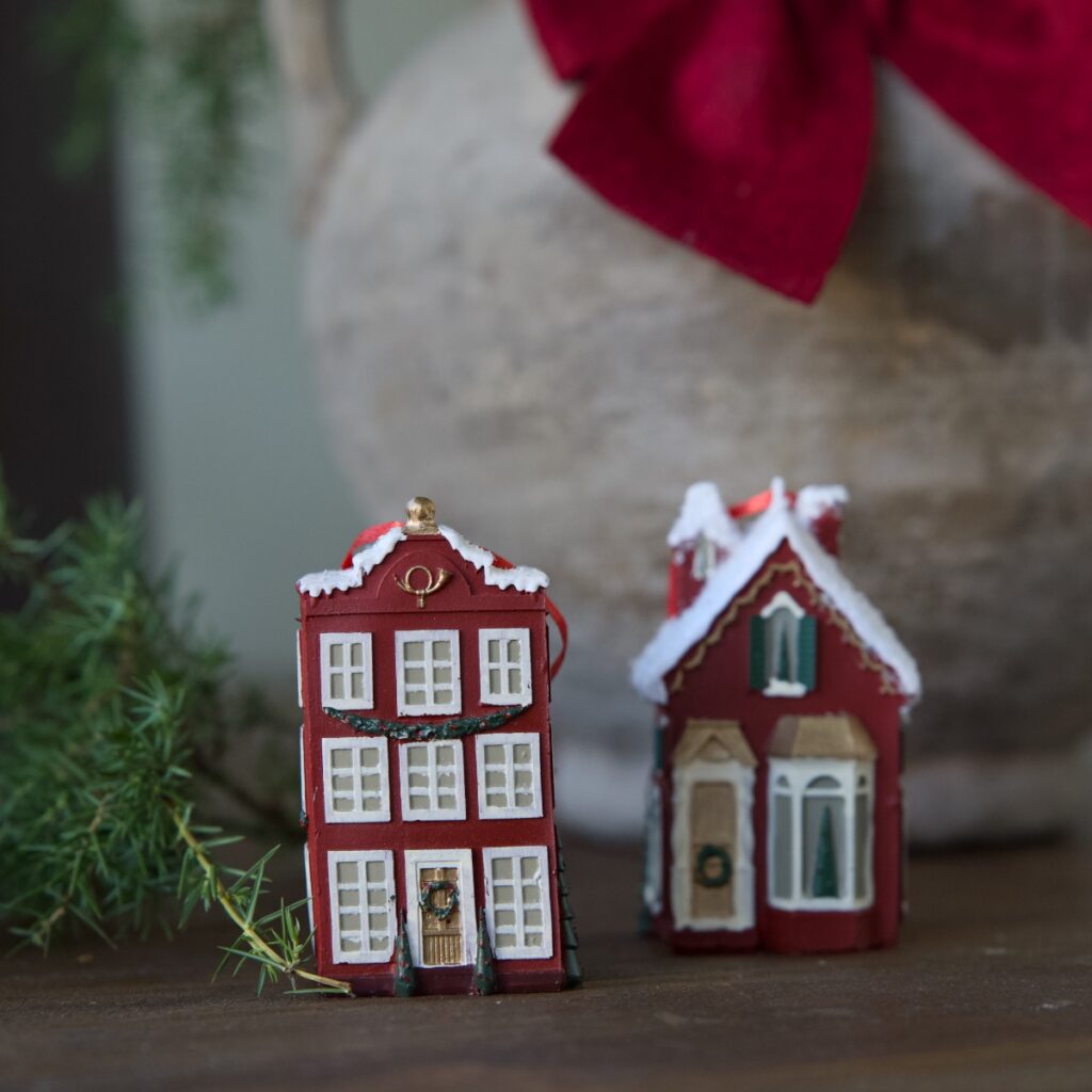Rött miniatyrstadshus som juldekoration från Hemlängtan, fotograferat i en varm miljö med granris och juldetaljer.