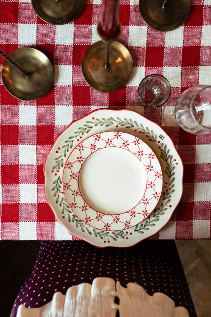 ulservis med röda och gröna detaljer på rödvitrutig duk – lantlig juldukning med mässingsljus.
