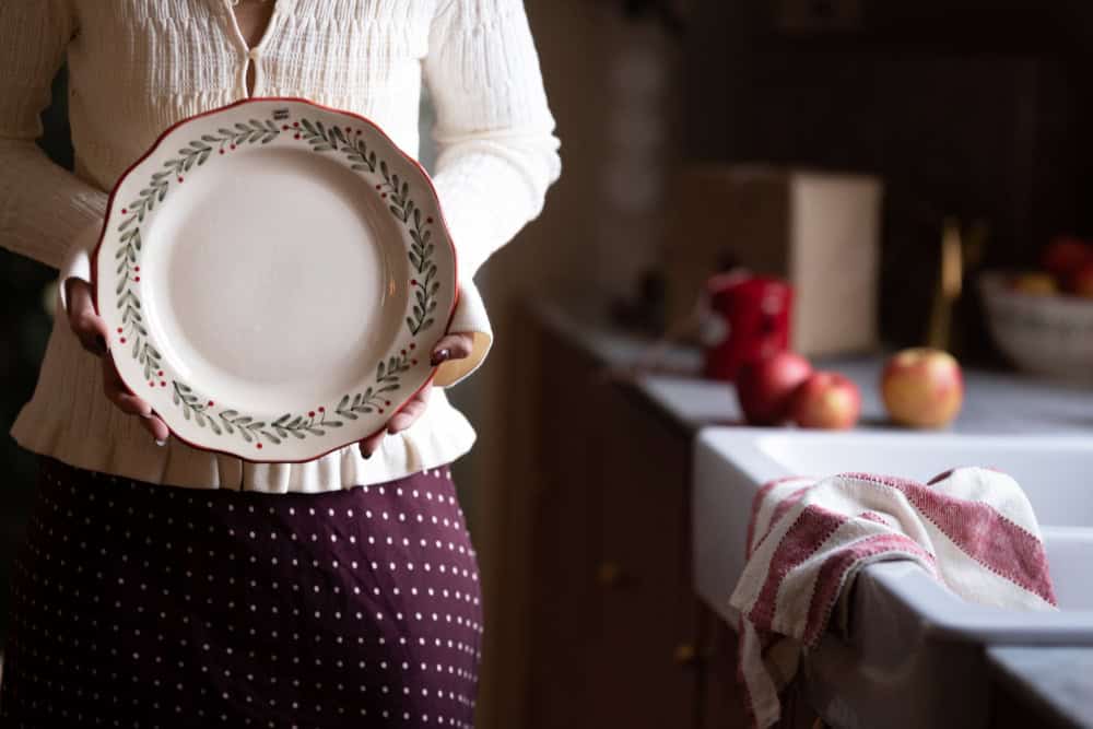 Kvinna håller tallrik ur julservis med grön och röd dekor – lantlig julstil från Hemlängtan.