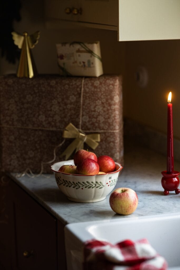 Skål med röda äpplen, tänd ljus och inslagna paket – enkel juldekoration i lantlig stil.
