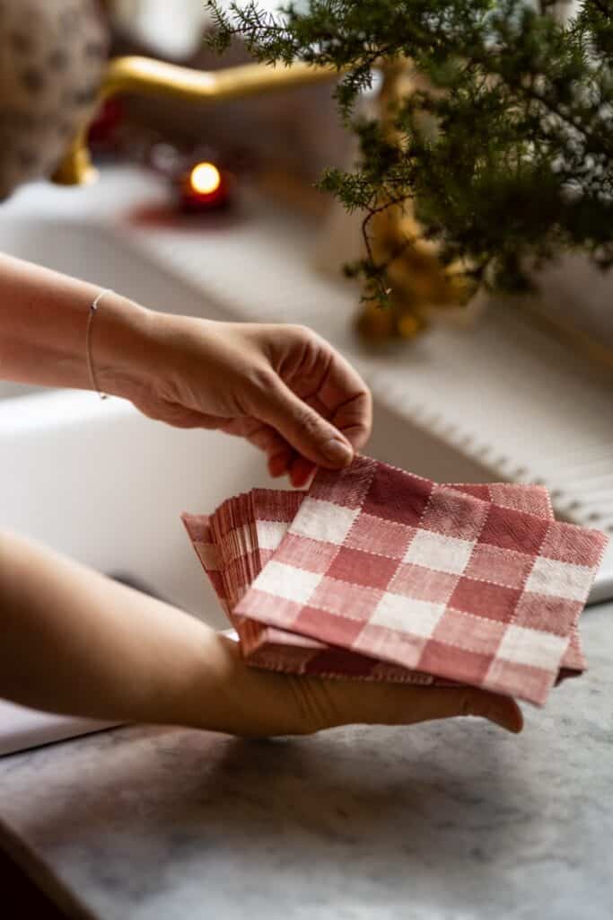 Hand som håller rödvitrutiga servetter – detalj av lantlig juldukning i klassisk stil.