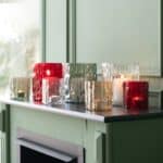 Flera glaslyktor i olika färger tända på en grön hylla, Valdir-serien.