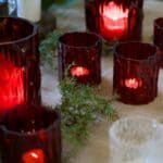 Tända röda glaslyktor från Valdir-serien på dukad yta med gröna kvistar.