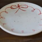 Närbild av assiett i vit keramik med handmålad röd rosett runt kanten.