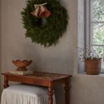 Fruktskål i naturfärgad rotting på fot placerad på litet bord i varm miljö med grön krans på väggen