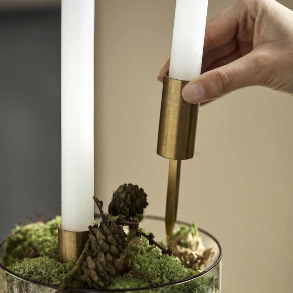 Mässingsfärgad ljushållare med spets placeras i mossa för att skapa ett dekorativt ljusarrangemang.