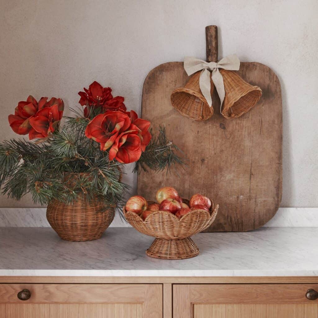 Rottingklockor med linneband ovanför skärbräda med äpplen och blommor i rottingkrukor