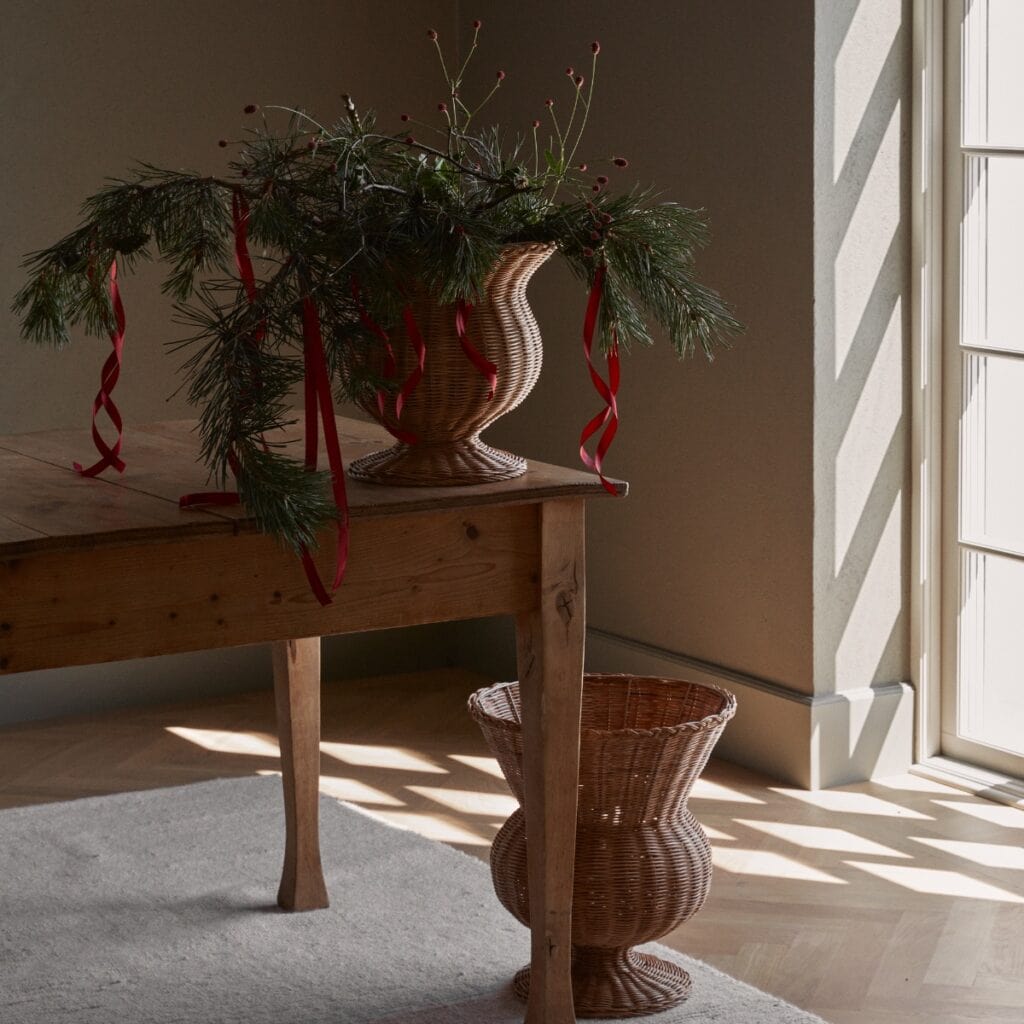 Urna i rotting dekorerad med granris placerad på träbord vid fönster