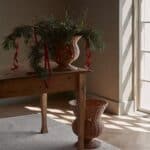 Urna i rotting dekorerad med granris placerad på träbord vid fönster