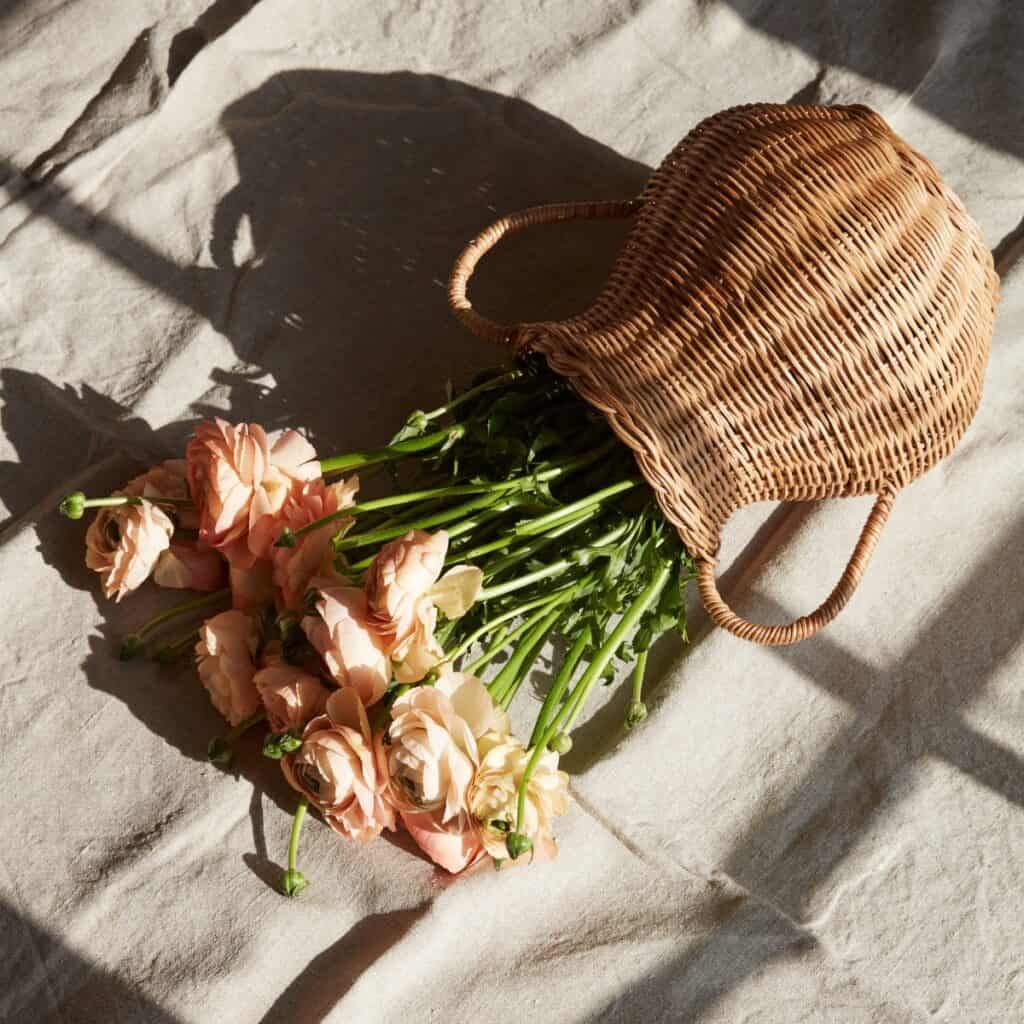 Vas i rotting med rosa blommor liggande på linneduk i varmt solljus.